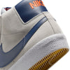 Close-up of the heel of a NIKE SB BLAZER MID WOLF GREY / MIDNIGHT NAVY sneaker, featuring an orange logo, textured sole detail, intricate stitching, and Zoom Air cushioning. Ideal for skateboarders who prioritize both style and performance.