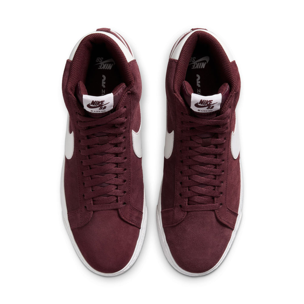 A pair of maroon high-top nike NIKE SB BLAZER MID BURGUNDY CRUSH / SUMMIT WHITE with white soles, white Nike swooshes, and Zoom Air cushioning viewed from above.