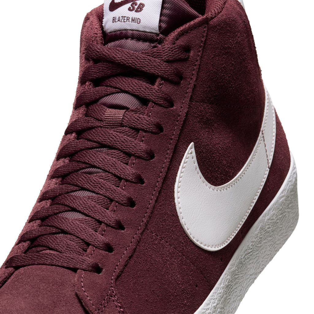 Close-up image of a maroon nike NIKE SB BLAZER MID BURGUNDY CRUSH / SUMMIT WHITE sneaker featuring a suede upper, white swoosh logo, white textured sole, and maroon laces.