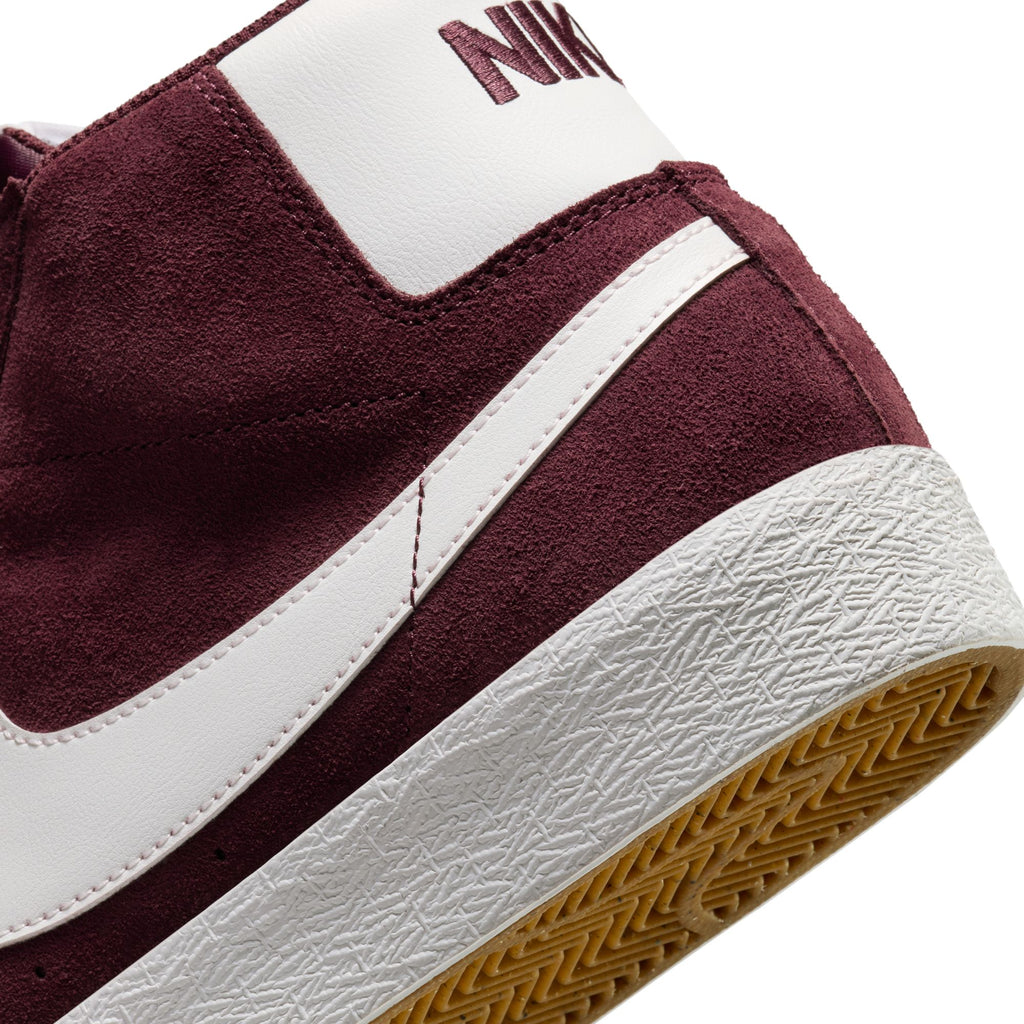 Close-up of a maroon and white NIKE SB BLAZER MID BURGUNDY CRUSH / SUMMIT WHITE sneaker showing the heel and a portion of the rubber outsole. The sole has a textured pattern with Zoom Air cushioning, and the nike logo is partially visible on the white heel tab.