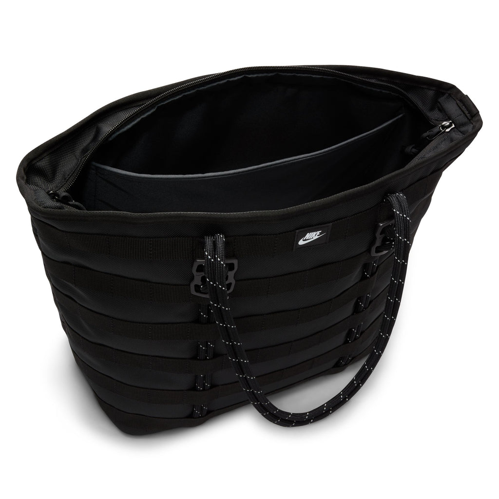The NIKE RPM TOTE (26L) BLACK features a zippered main compartment, black webbing details, rope-style handles, and a small Nike logo—ideal as a laptop bag or an everyday tote made from recycled polyester.