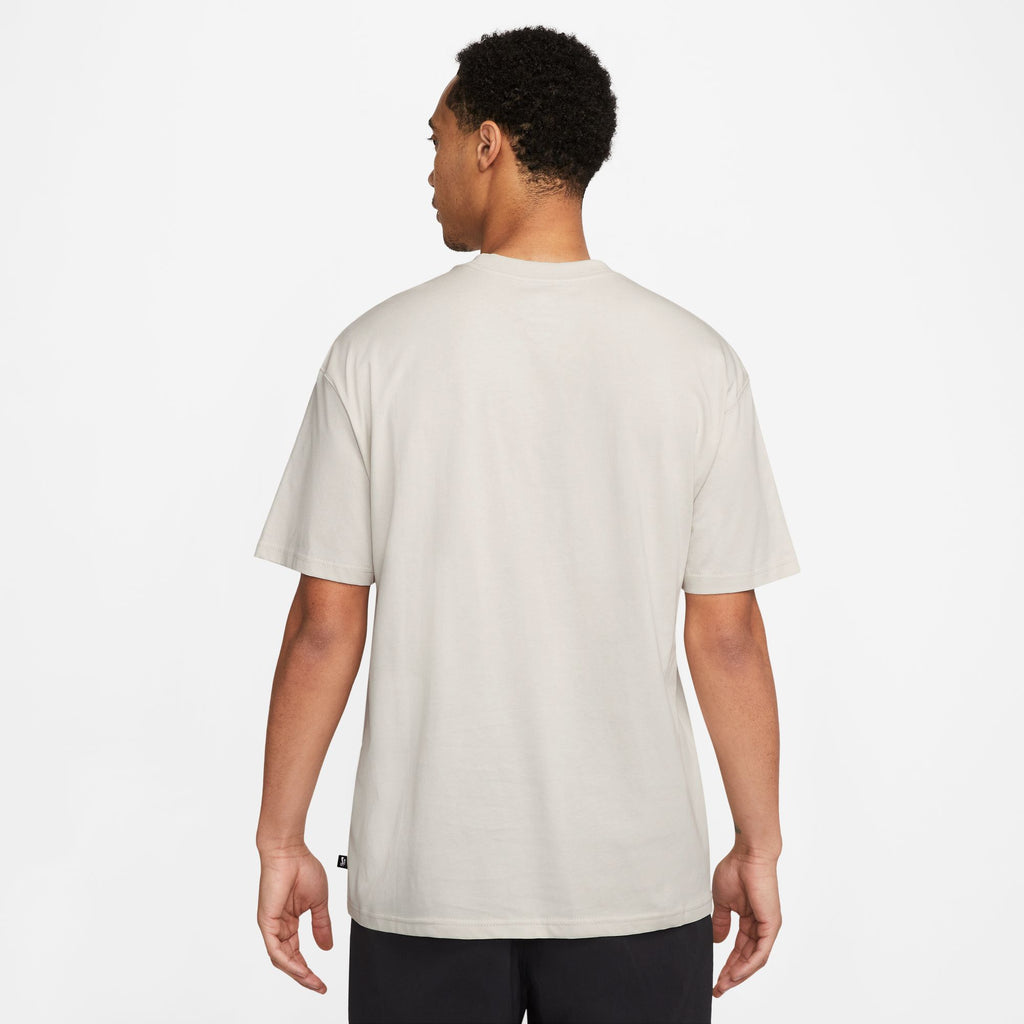 The back view of a man wearing a nike SB 'SPORTS GUY' SKATE TEE LIGHT BONE t-shirt in beige.