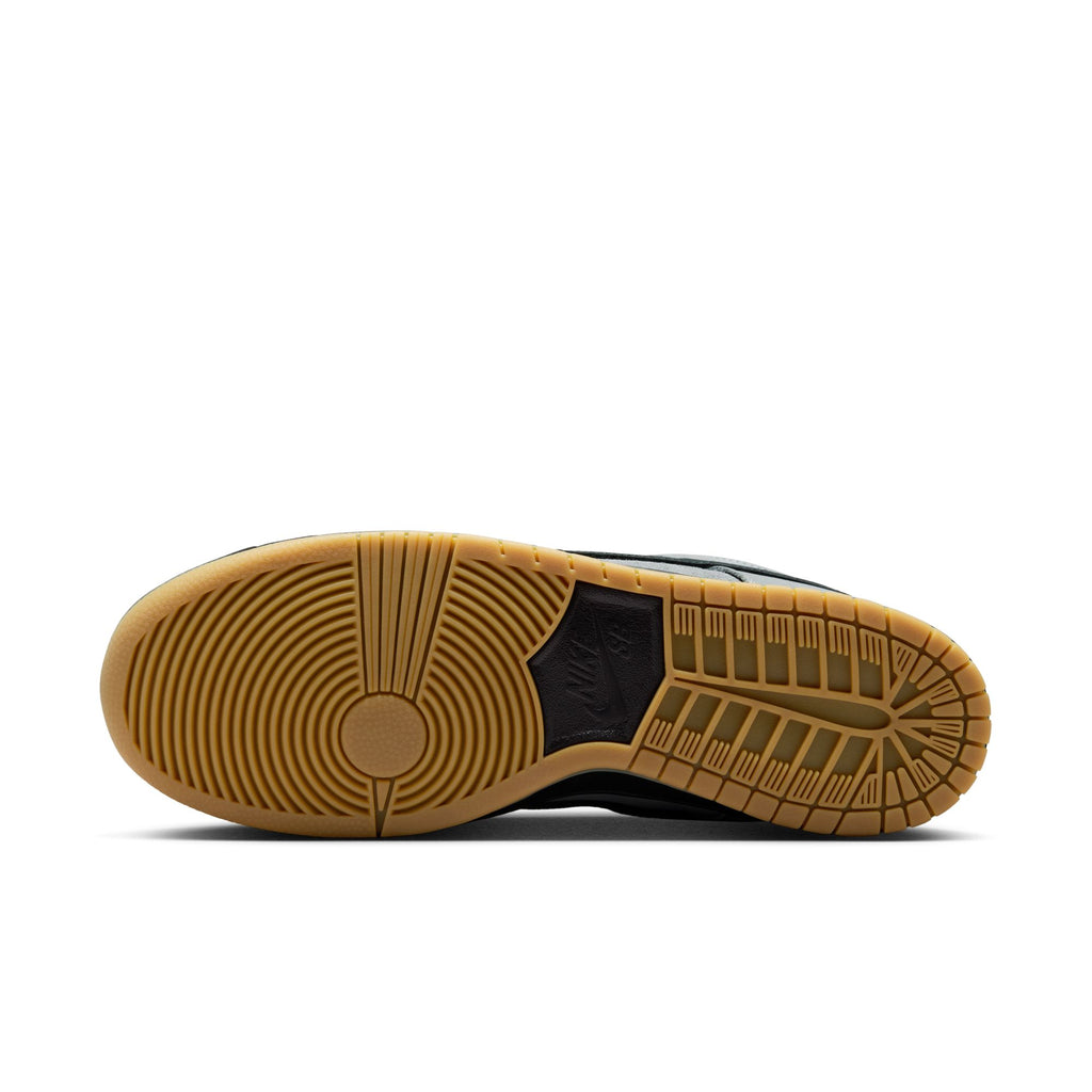 The image displays the gum rubber outsole of the NIKE SB DUNK LOW PRO in Cool Grey/Black, featuring circular and linear tread patterns for grip and traction—perfect for skateboarding.
