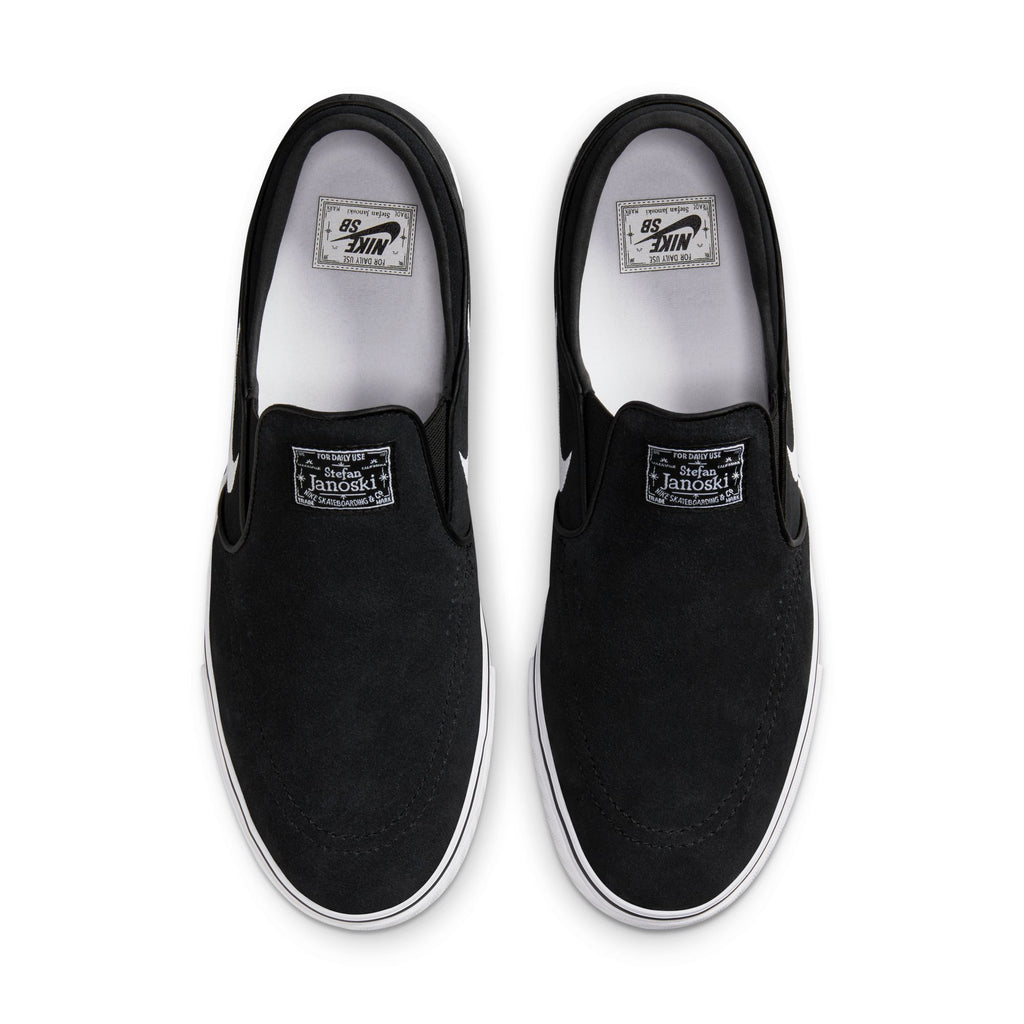 The NIKE SB JANOSKI+ SLIP in Black/White-Black-Black combines heritage basketball DNA with cupsole durability, featuring a black slip-on design, white soles, and "Nike SB" and "Stefan Janoski" labels on the inner soles.