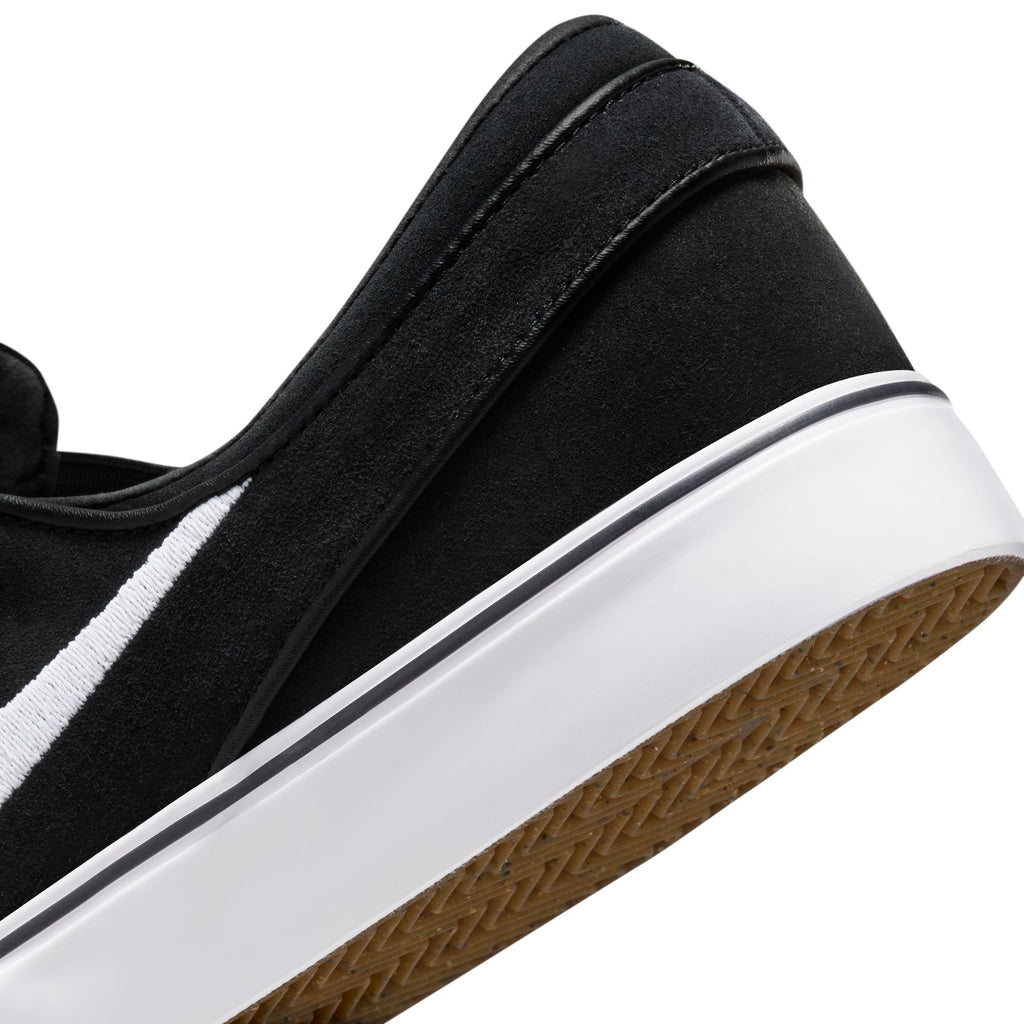 Close-up of the Nike SB Janoski+ Slip in Black/White, showcasing a black sneaker with a white stripe, thick white sole, skate-specific tread, and brown textured bottom.