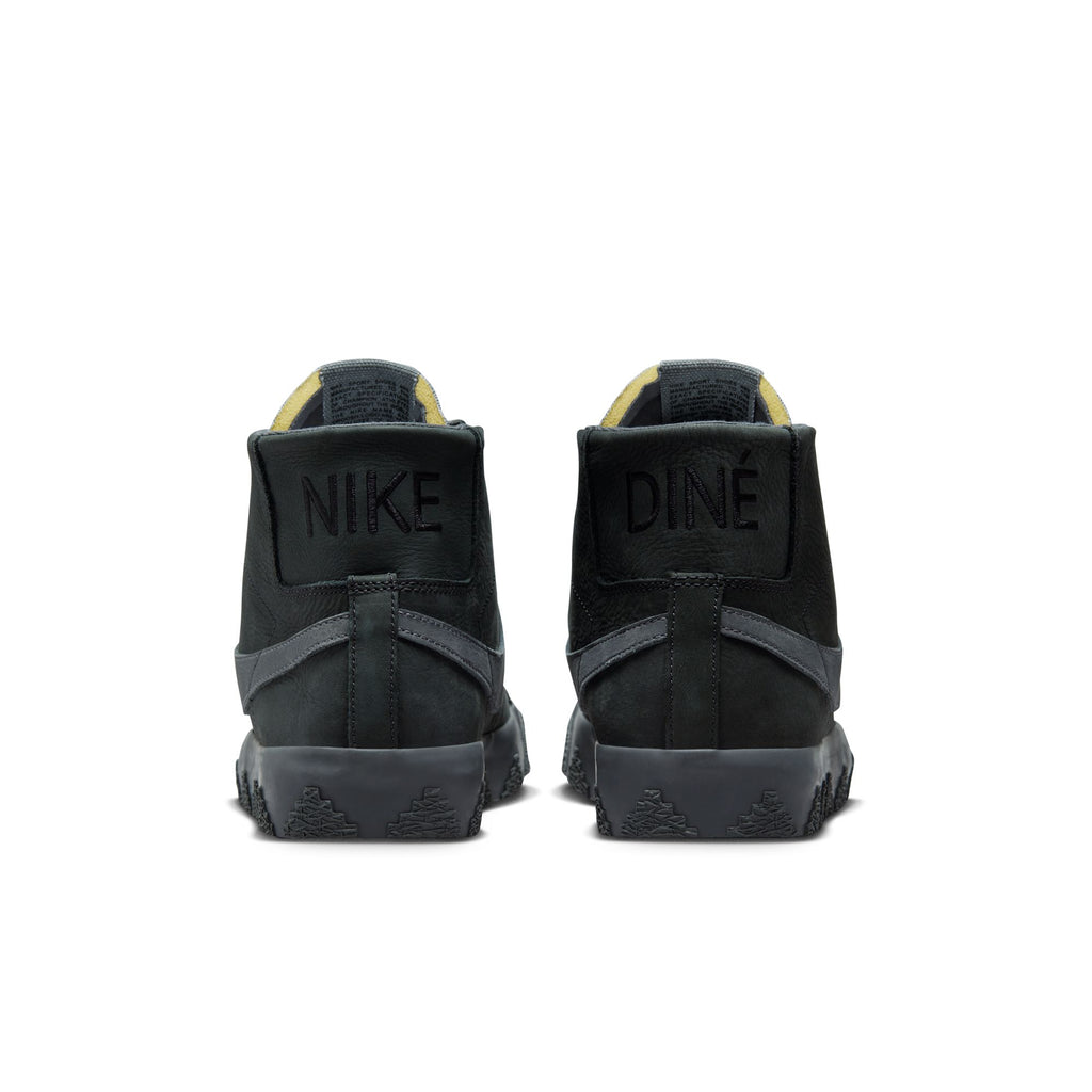 Rear view of a pair of black high-top nike sneakers showing the words "NIKE" on the left shoe and "DINE" on the right shoe. These nike NIKE SB X DI'ORR GREENWOOD BLAZER MID DECON ANTHRACITE / DARK GREY SMOKE skate shoes feature renowned Zoom Air cushioning for added comfort during every trick and turn.