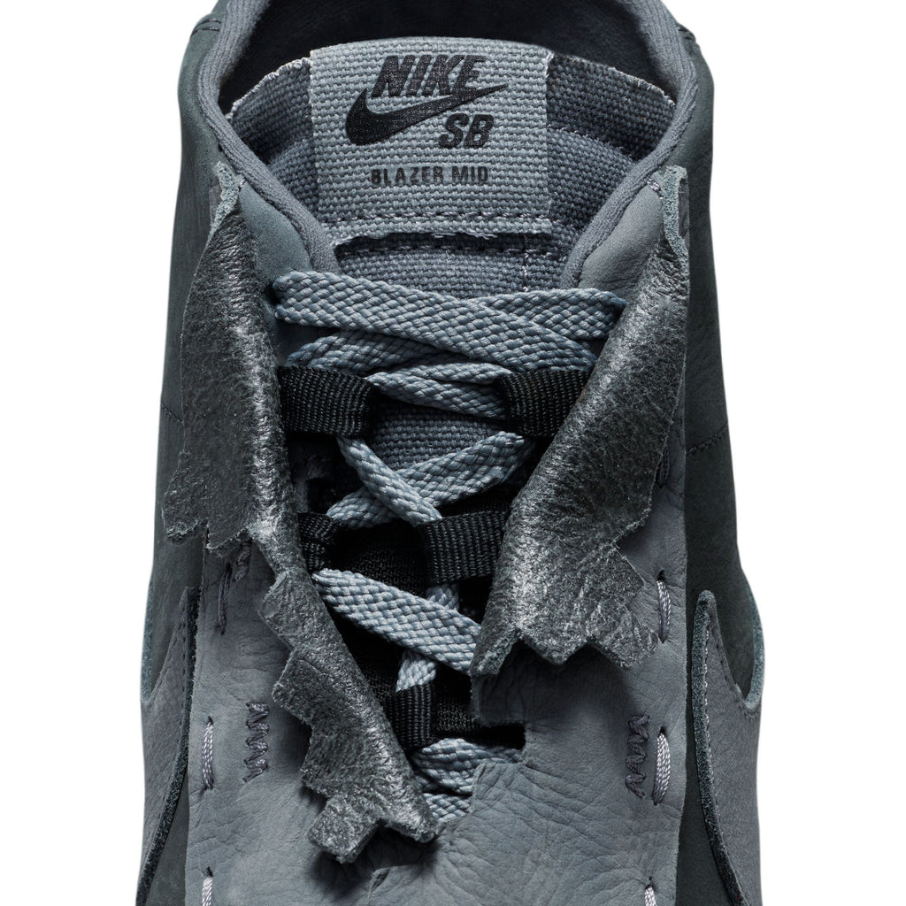 Close-up of the upper part of a grey Nike SB X Di'orr Greenwood Blazer Mid Decon Anthracite / Dark Grey Smoke sneaker, showing the lacing system, tongue with logo, and textured details around the eyelets. These skate shoes feature Zoom Air cushioning for enhanced comfort and performance.