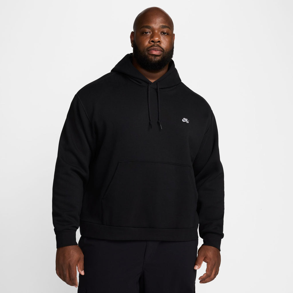 A man wearing a black Nike SB Essentials Logo Fleece Hoodie, featuring a small logo on the chest, stands against a plain white background.