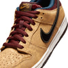 Close-up of the NIKE SB DUNK LOW PRO CELESTIAL GOLD/BLACK-DARK TEAM RED sneaker by Nike, showcasing a vintage treatment with a black swoosh, dark team red laces, and a white sole.