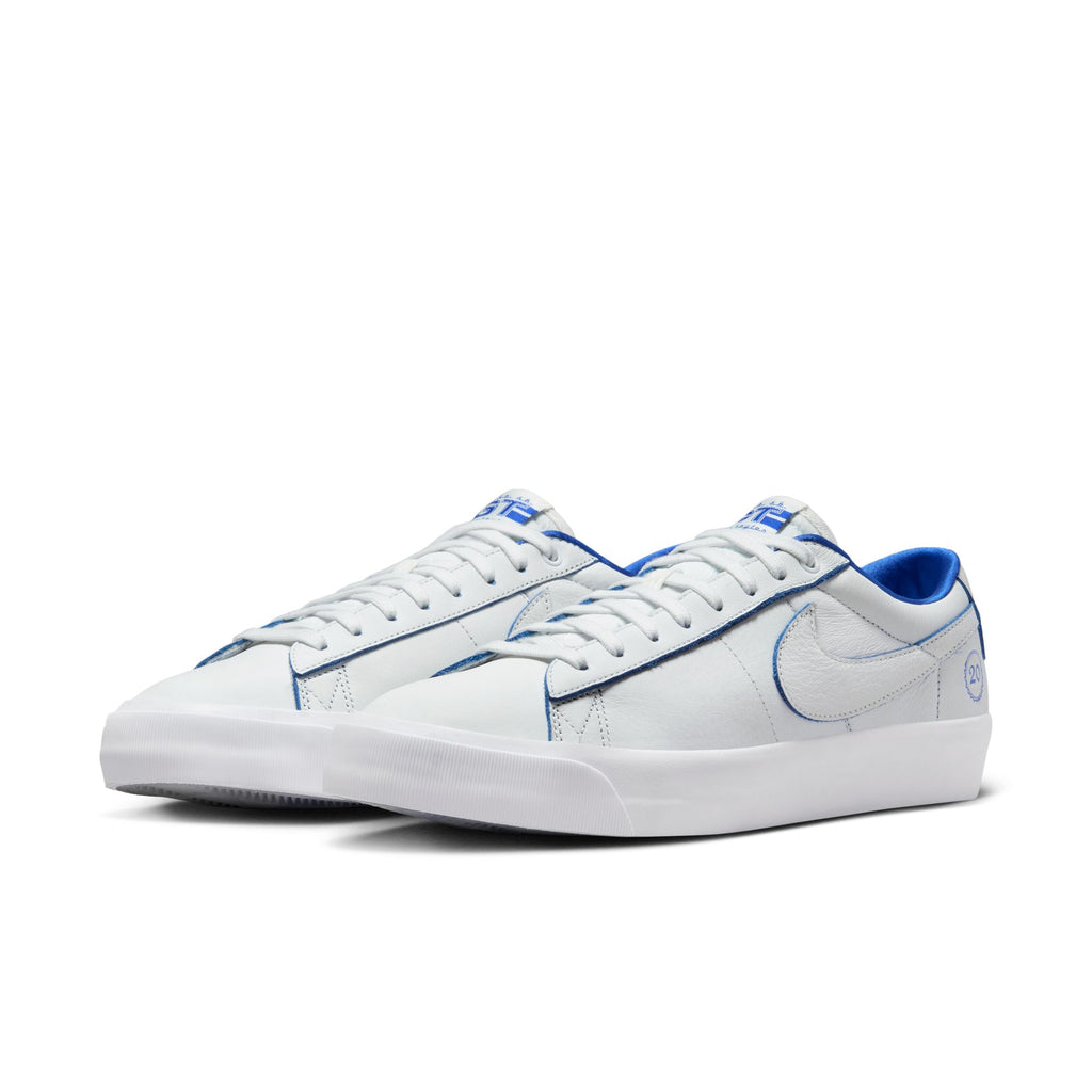 The NIKE SB BLAZER LOW PRO GT "20 YEARS" sneakers in Summit White and Game Royal, featuring Air Zoom cushioning and the Swoosh logo on a plain background.