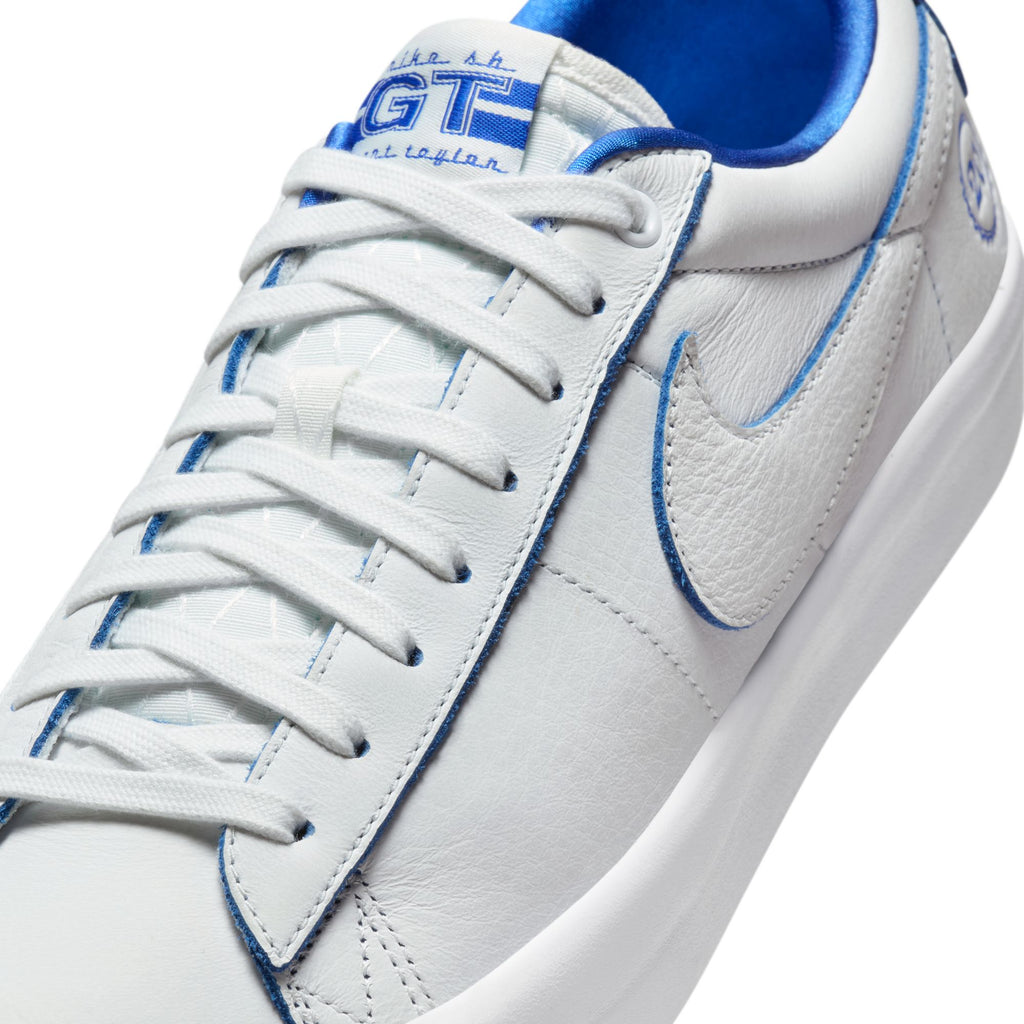 Close-up of the NIKE SB Blazer Low Pro GT "20 Years" sneaker in Summit White and Game Royal, showcasing its swoosh logo on the side and "GT" text on the tongue. This design provides style and comfort, embodying skateboarder Grant Taylor's signature look.