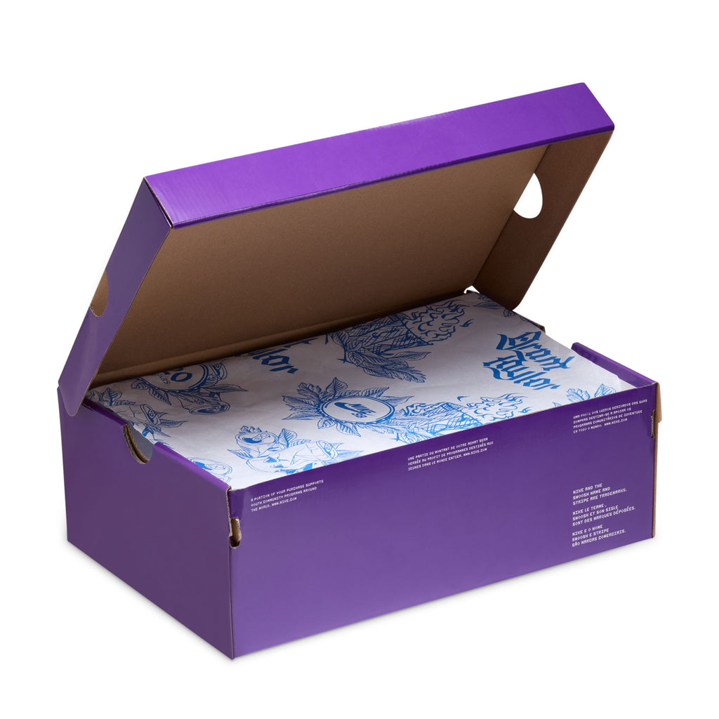 A purple shoebox with a partially open lid, revealing blue and white tissue paper inside, cradles the NIKE SB Blazer Low Pro GT "20 Years" in Summit White/Game Royal, featuring Air Zoom cushioning for ultimate comfort.