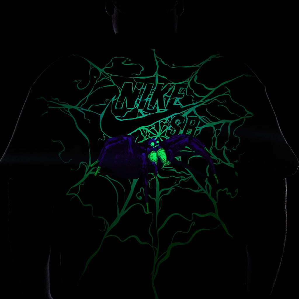 The NIKE SB SPIDER TEE BLACK GLOW IN THE DARK, by Nike, is a black skate T-shirt featuring a neon green logo with a glowing purple spider design, perfect for adding an edgy vibe to your look.