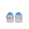 Rear view of a pair of NIKE SB X NICOLE HAUSE DUNK LOW PRO sneakers in white with blue accents and black "NIKE" text on the heel, featuring a chain on the left shoe. These stylish classics from Nike offer comfort in every step.