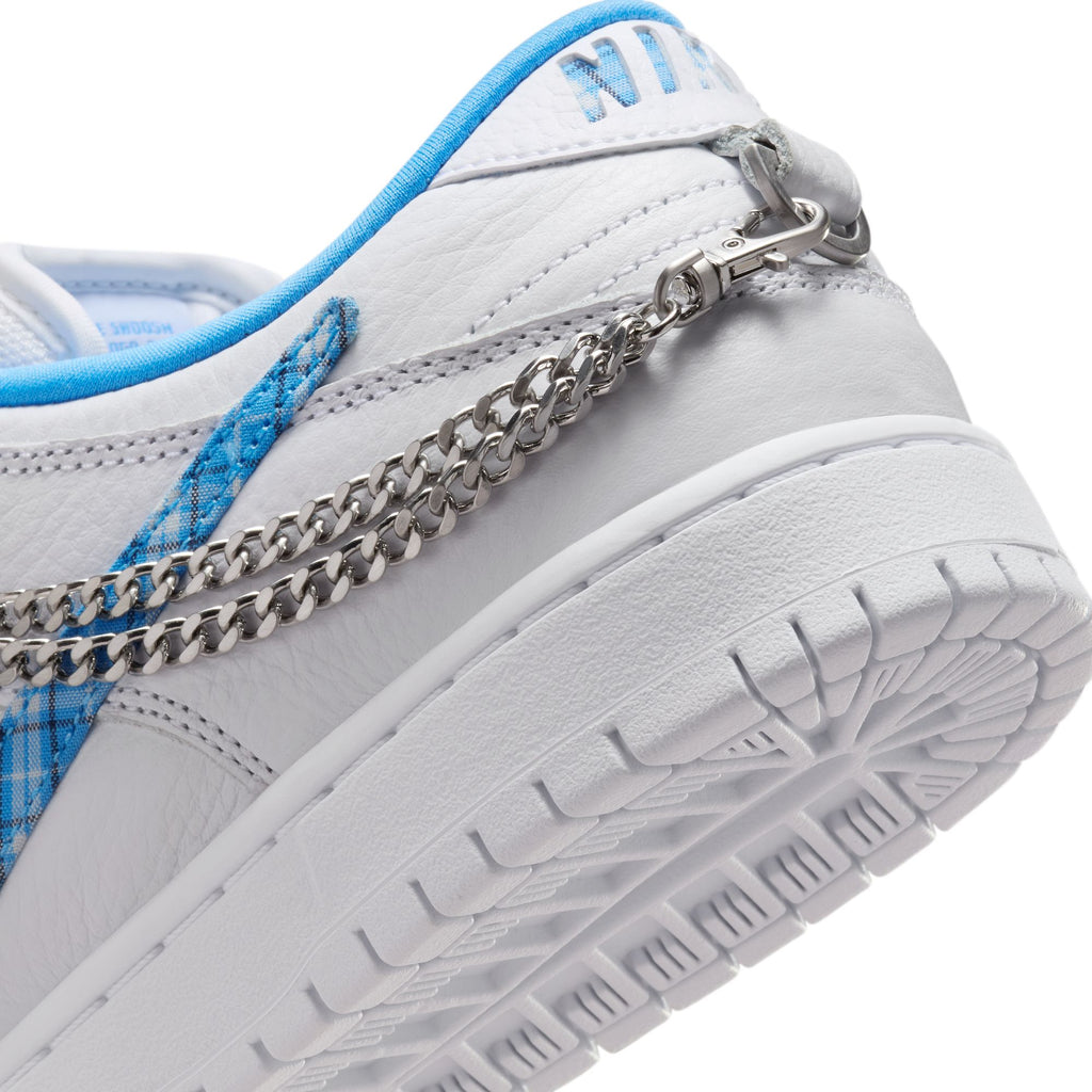 Close-up of the NIKE SB X NICOLE HAUSE DUNK LOW PRO, a white sneaker with blue accents and a silver chain detail, featuring Air Zoom cushioning. This shoe, reminiscent of the iconic NIKE SB Dunk Low style, has a textured white sole and visible stitching.