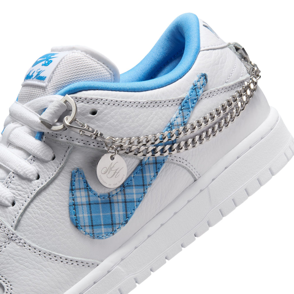 Close-up of a white NIKE SB X Nicole Hause Dunk Low Pro sneaker showcasing a blue plaid Nike logo and a silver chain with a round charm attached, designed for maximum comfort with Dunk Low style and Air Zoom cushioning.