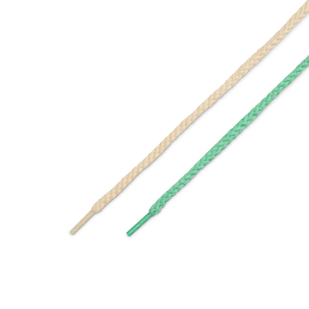 Two shoelaces, beige and green with plastic aglets, are displayed side by side on a white background—paying homage to the Southwest heritage behind the nike SB Rodeo Dunk Low Tourmaline/Baroque Brown-Monarch.