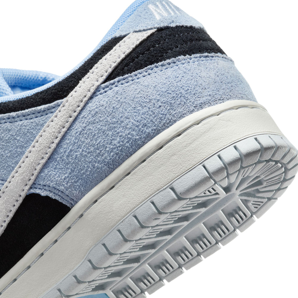 Close-up of the NIKE SB DUNK LOW PRO ALUMINUM / BLACK-FOOTBALL GREY shows premium materials with a textured sole for traction and a blue, black, and white suede upper featuring elegant white stripe detailing.