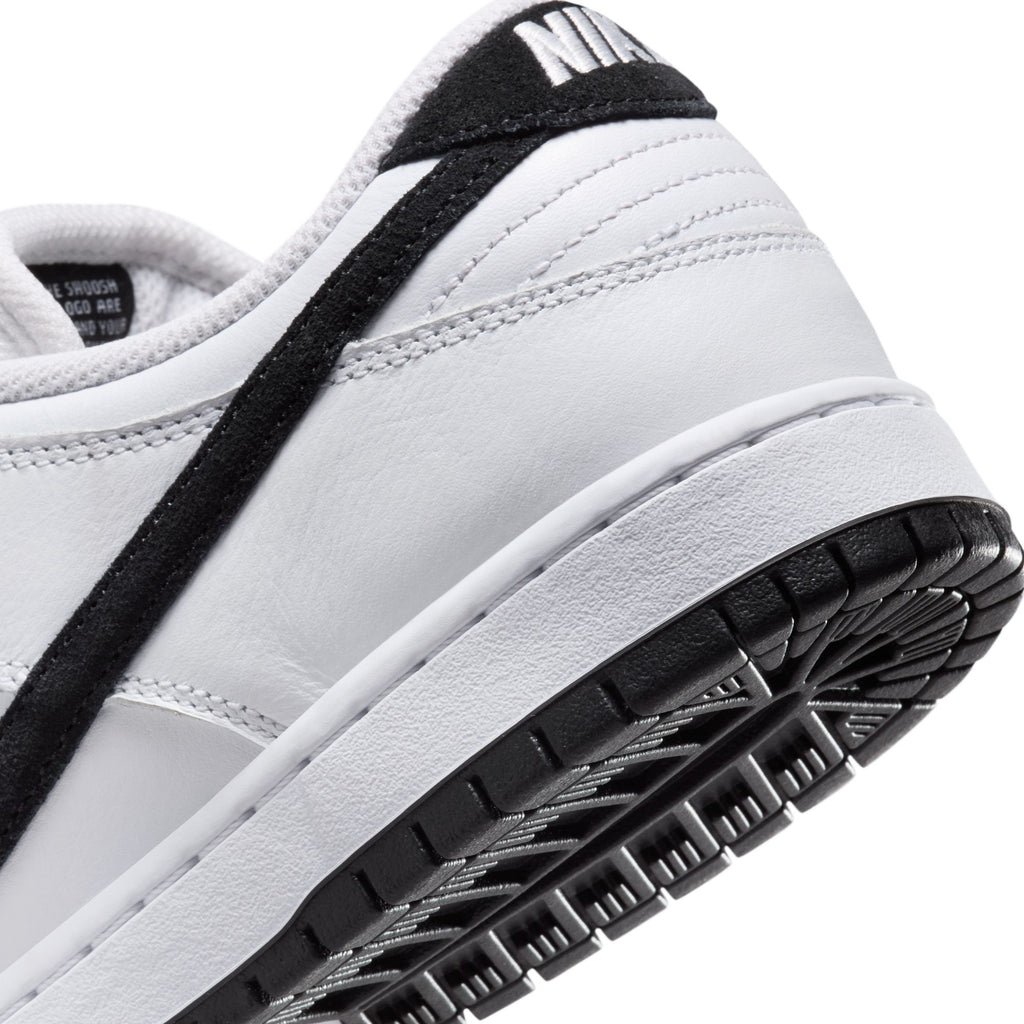 Close-up of a NIKE SB DUNK LOW PRO WHITE/BLACK-WHITE-BLACK sneaker featuring a black swoosh, black sole, foam midsole, visible stitching, and textured rear detail. Brand: nike.