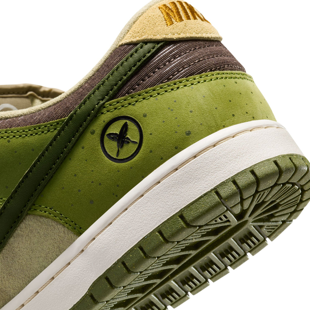 The RAFFLE WINNER NIKE SB YUTO "MATCHA" DUNK LOW PRO features a green heel with a brown and white sole, crafted from premium materials for durability. A small circular logo with a leaf design and textured pattern adorns the heel, highlighting its unique style.