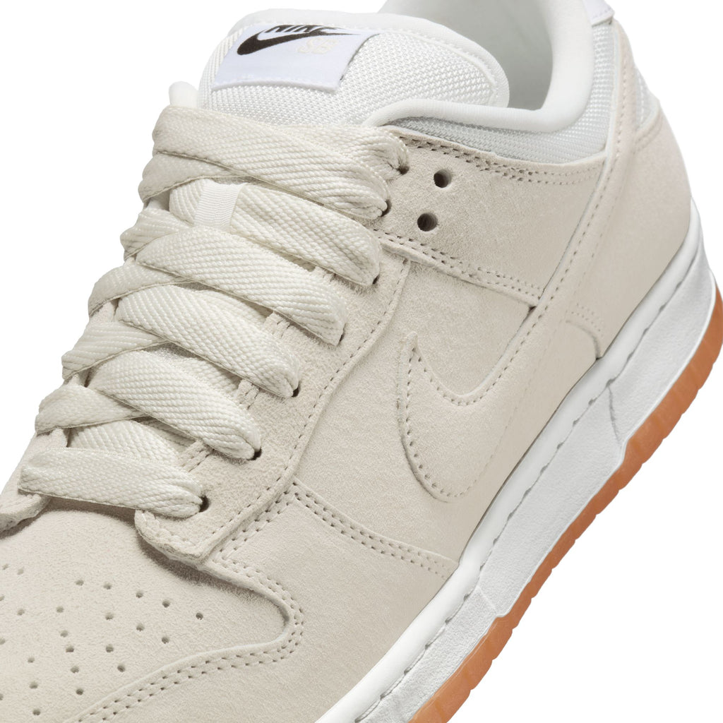Close-up of the NIKE SB DUNK LOW PRO B in Pale Ivory/Summit White by Nike, featuring white laces, a white midsole, gum rubber outsole, and visible Nike logos on the tongue and side.