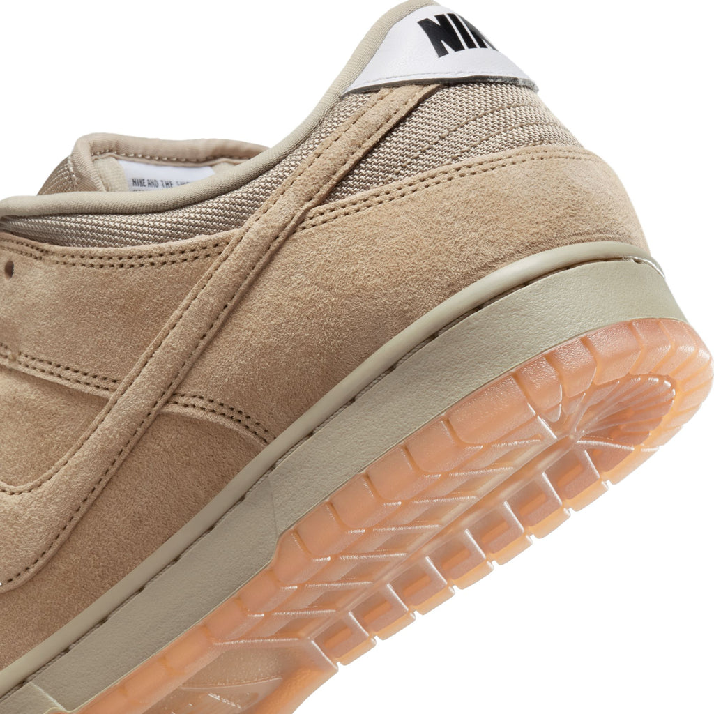 Close-up of a tan suede NIKE SB DUNK LOW PRO B sneaker with gum rubber sole, featuring the iconic Nike SB logo on a white label at the heel, finished in Parachute Beige for a stylish touch.