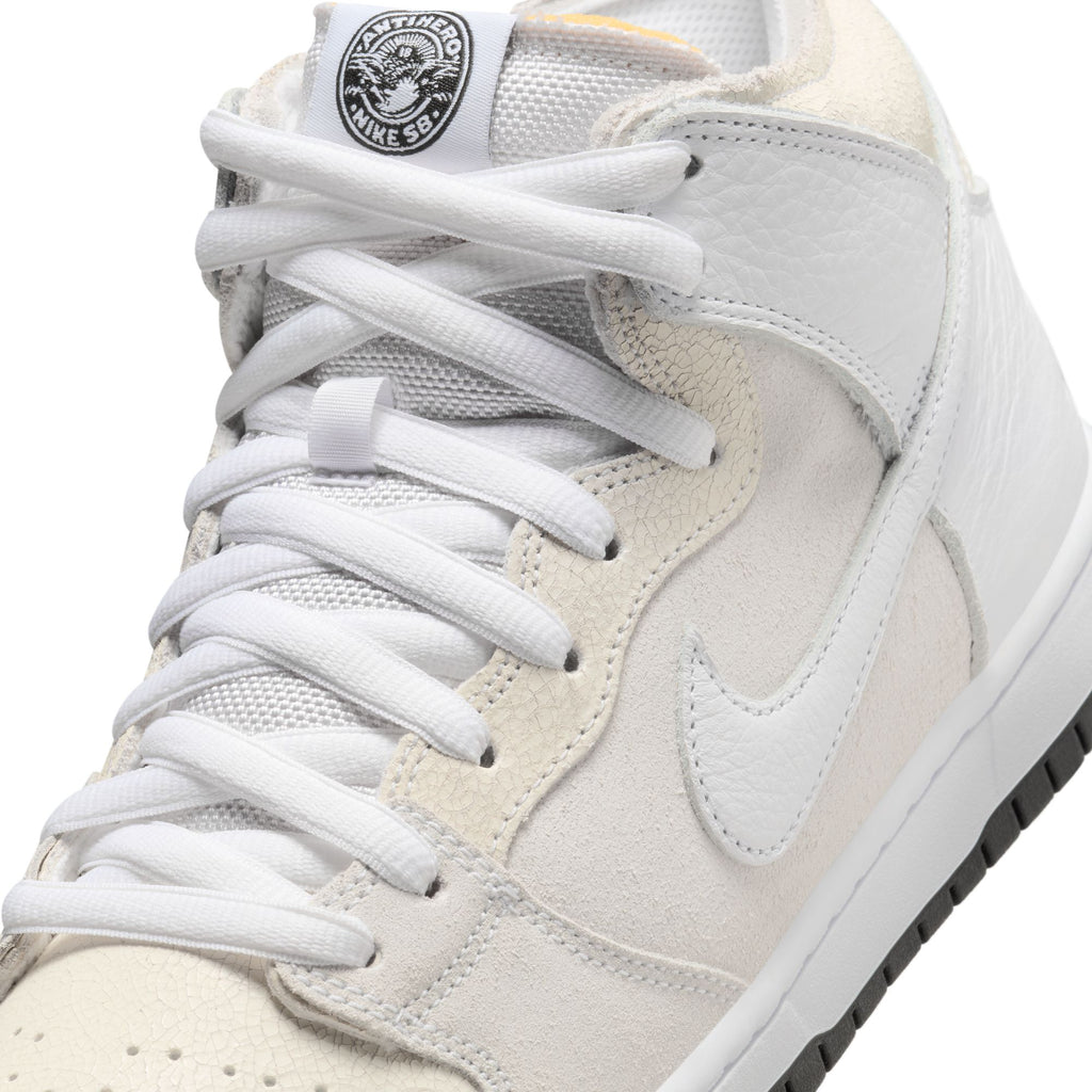 Close-up of the NIKE SB x ANTIHERO Dunk High White sneaker, showcasing black detailing on the tongue logo and complemented by white laces. This design reflects a timeless style reminiscent of collaborations like Antihero and Bluetile Skateboards.