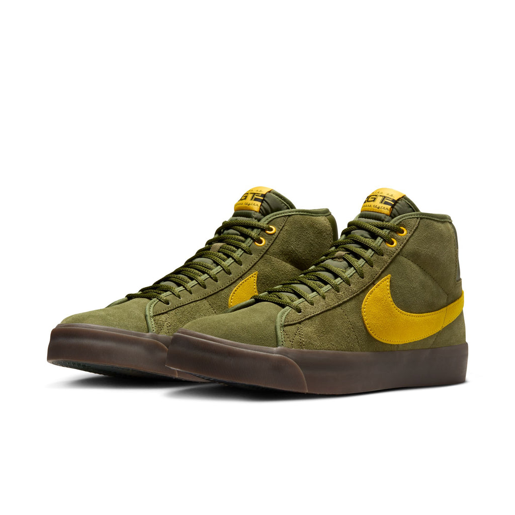 The NIKE SB x ANTIHERO Blazer GT Mid sneakers from Nike showcase a rough green color with an Amarillo swoosh, featuring a suede texture and brown rubber soles, making them ideal for skateboarding.