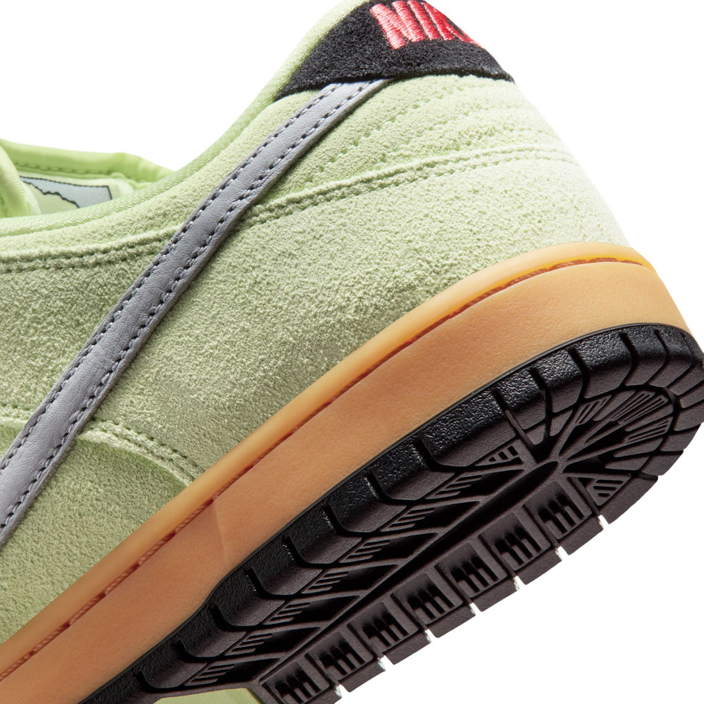 Close-up of the heel and sole of the NIKE SB DUNK LOW PRO VERDUGO MOUNTAIN by nike, showing light green suede, a grey stripe, gum midsole, black outsole, and red stitching on the heel inspired by Verdugo Mountain trails.