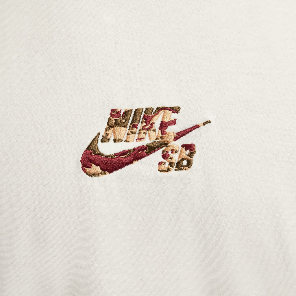 The NIKE SB CAMO CENTERED LOGO MAX90 TEE WHITE features a vibrant embroidered Nike logo with a camouflage pattern on a pristine white background, offering a dynamic look perfect for fans of the iconic Nike SB Sonics style.