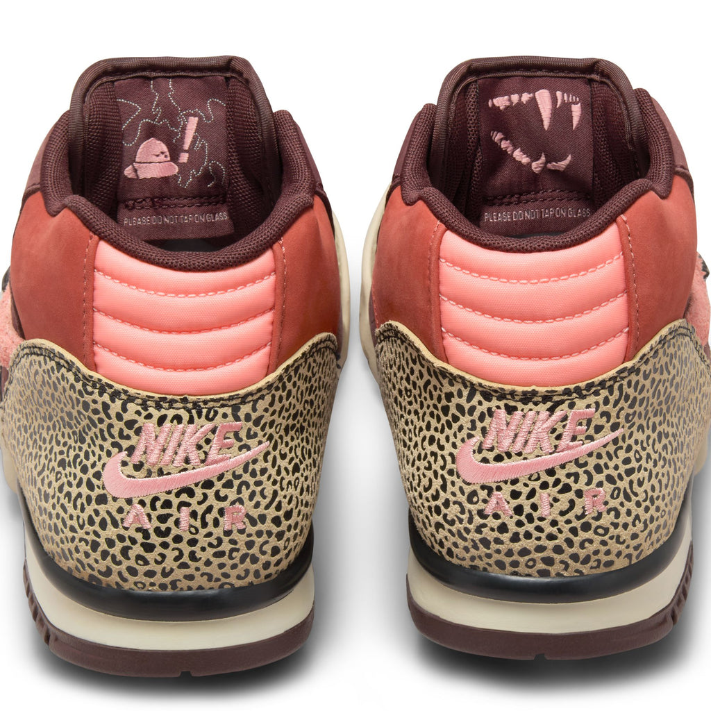 A pair of NIKE SB X ARTS-REC AIR TRAINER 1 shoes in Limestone/Pink Quartz with animal print on the heel, pink swooshes, and printed insoles are viewed from the back.