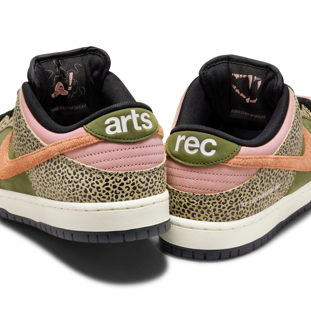 A pair of Nike SB x Arts-Rec Dunk Low Pro sneakers in khaki, amber brown, rough green, rust pink, black, and sail with "arts" on the left heel and "rec" on the right. Features animal print details and coral swooshes.