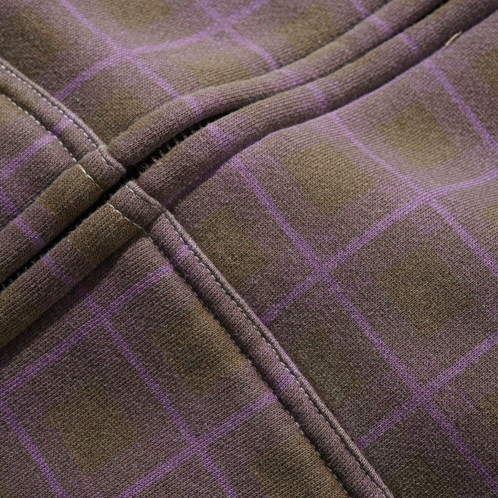 Close-up of the BUTTER ERUPTION ZIP-THRU HOODIE PLAID by Butter Goods, featuring brown fabric with a purple plaid pattern, intersecting seams, and detailed stitching for a cozy fleece finish.