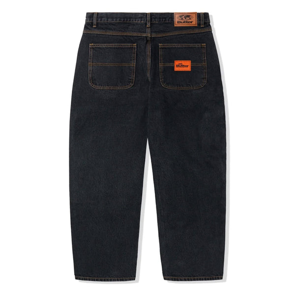 A pair of BUTTER GOODS SANTOSUOSSO DENIM PANT WASHED BLACK jeans with an orange patch on the back and a baggy fit.