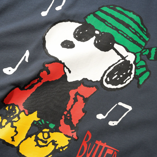 The BUTTER GOODS X PEANUTS MUSIC TEE SLATE by Butter Goods features a cartoon dog in colorful clothes, green striped headscarf, sunglasses, and musical notes with "BUTTER" at the bottom, printed on a 100% cotton tee.