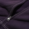 A close-up of the partially unzipped silver zipper on dark purple fabric with white stitching highlights the detail of the Butter Goods BUTTER SKETCH ZIP-THRU HOODIE EGGPLANT.
