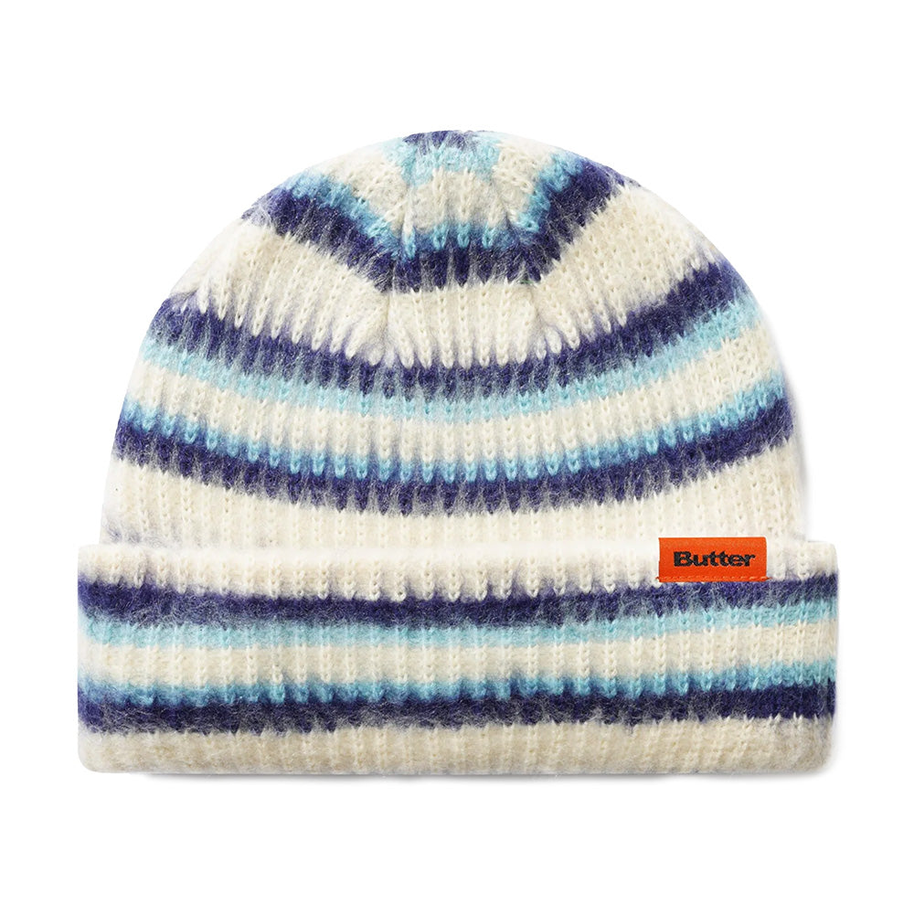 The Butter Goods BUTTER SWIPE BEANIE CREAM features a white jacquard stripe design with blue and navy stripes, a folded brim, and an orange "Butter" label.
