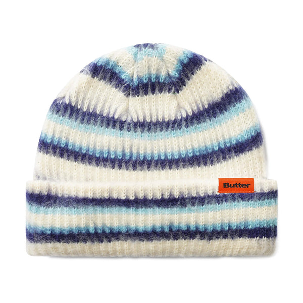The Butter Goods BUTTER SWIPE BEANIE CREAM features a white jacquard stripe design with blue and navy stripes, a folded brim, and an orange "Butter" label.