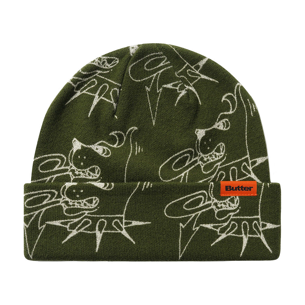 The BUTTER CANINE BEANIE FATIGUE by Butter Goods is a green acrylic fold beanie with white abstract cartoon designs and an orange "Butter" label on the front cuff.