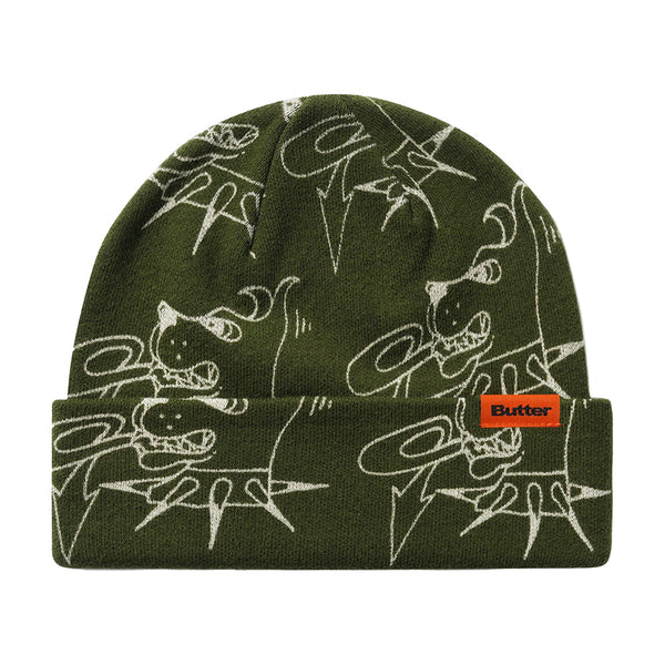 The BUTTER CANINE BEANIE FATIGUE by Butter Goods is a green acrylic fold beanie with white abstract cartoon designs and an orange "Butter" label on the front cuff.