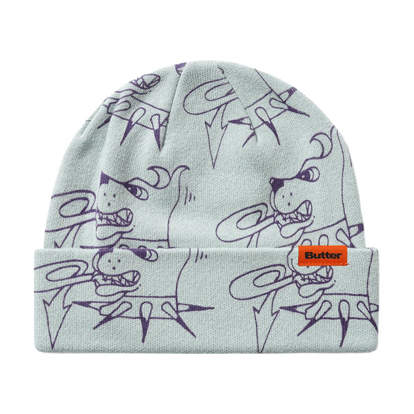 The Butter Goods BUTTER CANINE BEANIE GREY features a light gray knit, playful purple cartoon doodle pattern, and an orange "Butter" label on the front cuff—adding fun to your winter style.