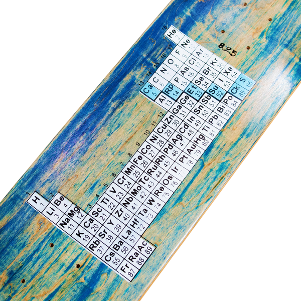 The CARPET BACTERIA skateboard deck from Carpet Co. features a large numeral "1" composed of periodic table elements' symbols against a blue and wood grain background. It boasts screen-printed graphics for enhanced durability and is available in various stains that complement its base colors.