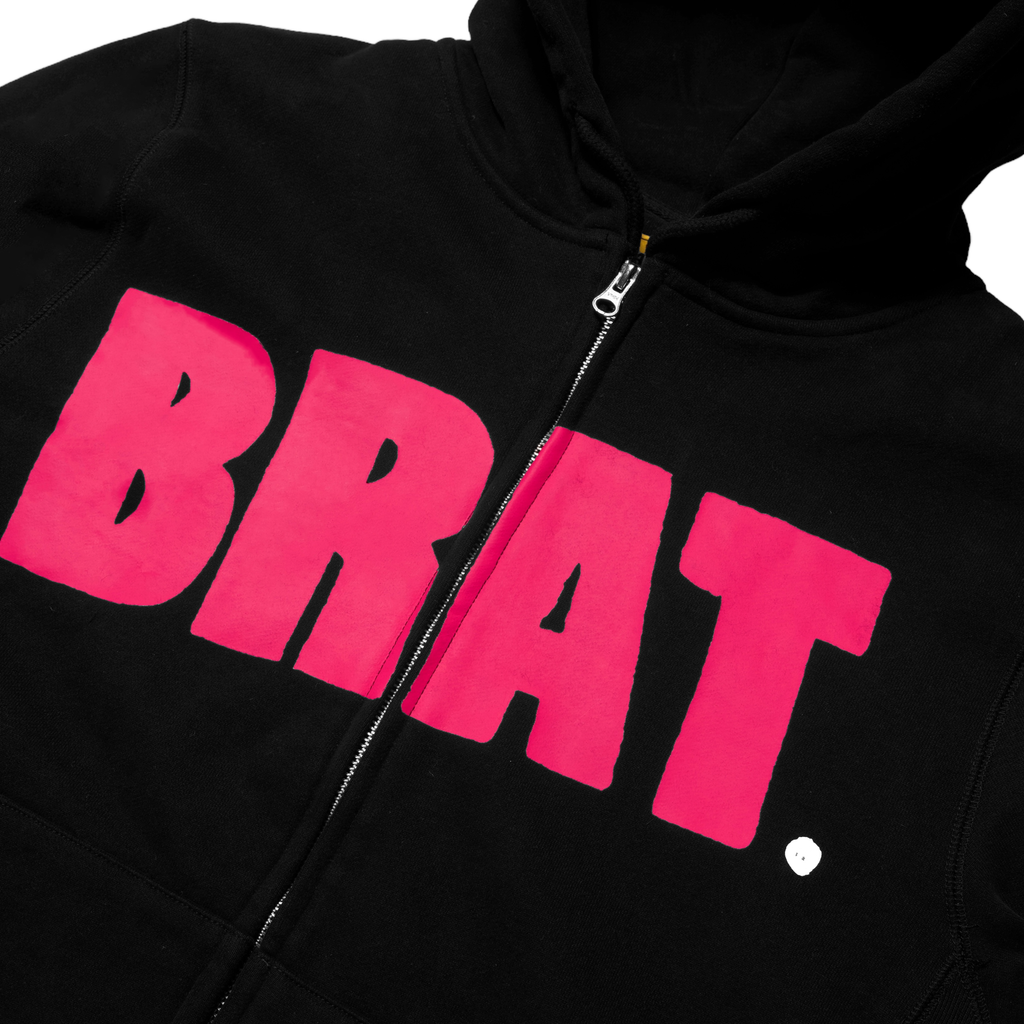 Carpet Co. black hoodie with a bright pink "brat" print on the chest, featuring a zip closure and a drawstring hood.