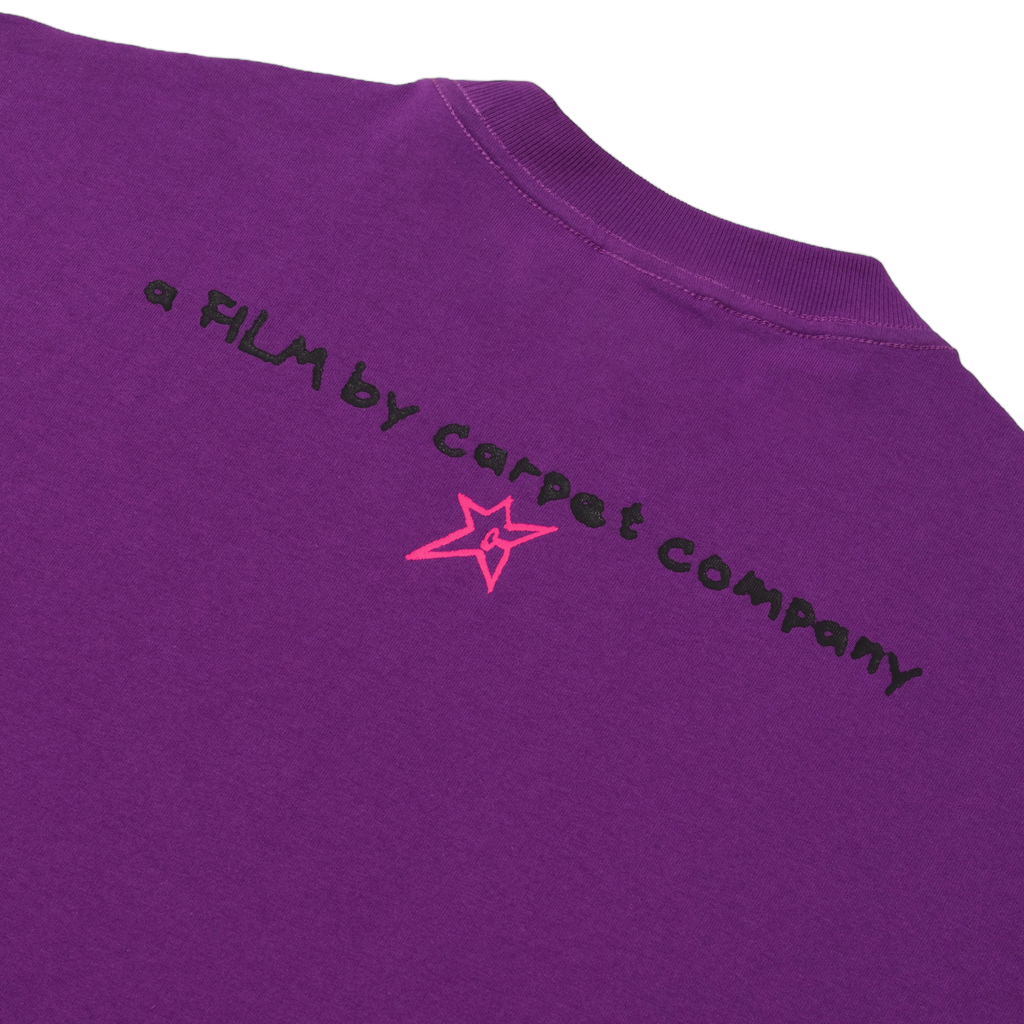 Close-up of purple Carpet Co. Brat Tee with text "a film by Carpet Co" and a pink star graphic on the upper back.