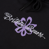 Close-up of the WELCOME X Britney Flower Pigment-Dyed Hoodie Black with "Britney Spears" written in white script and a purple floral design in the background, much like the elegant patterns seen on our Britney Daisies Tee.