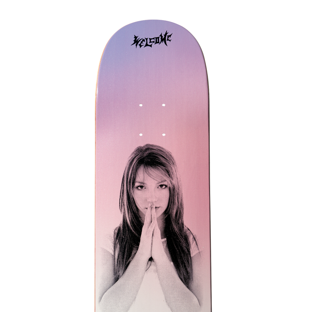 The WELCOME X BRITNEY BELIEVE skateboard deck from WELCOME features a person with folded hands against a gradient pink and purple background, accented with Pink Glitter. The word "Welcome" is printed at the top in a stylized font.