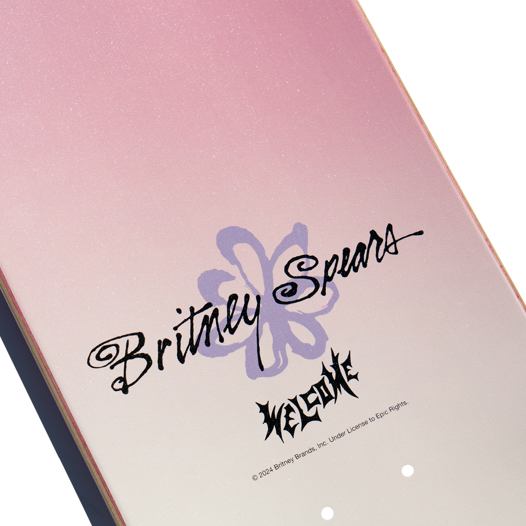 A pink skateboard deck titled "WELCOME X BRITNEY BELIEVE" features "Britney Spears" and "Welcome" printed on it alongside a central flower graphic with a hint of pink glitter. The text "© 2023 Britney Brands, Inc." at the bottom adds a nostalgic touch reminiscent of "Britney Baby One More Time” vibes.