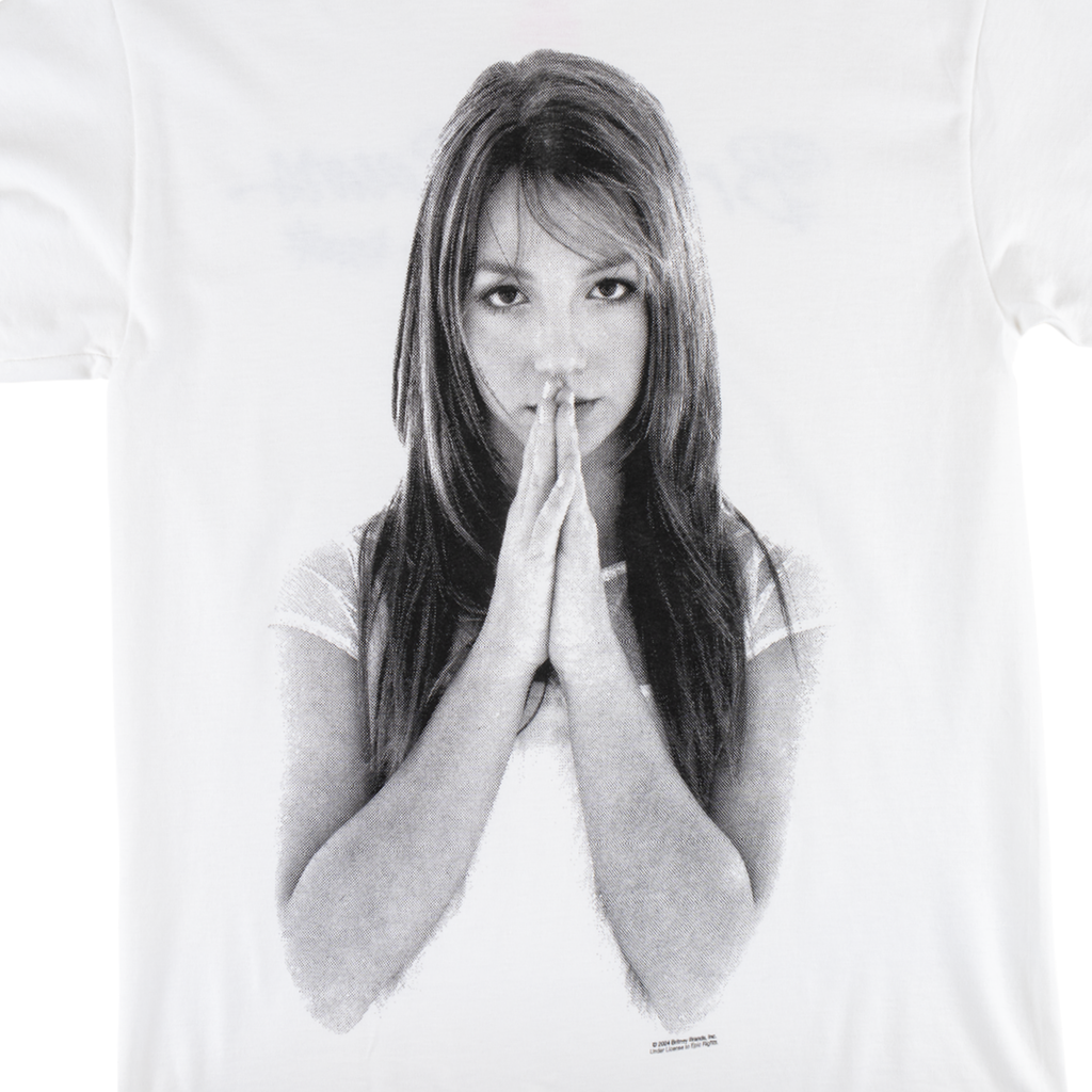 A black-and-white image of a person with long hair printed on a white WELCOME X BRITNEY BELIEVE TEE by WELCOME. The person is holding their hands together near their face.