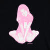 The WELCOME X BRITNEY FLOWER TEE BLACK by WELCOME showcases a pink-tinted image of a smiling person sitting cross-legged against a black background, capturing an essence reminiscent of a classic cowgirl theme.