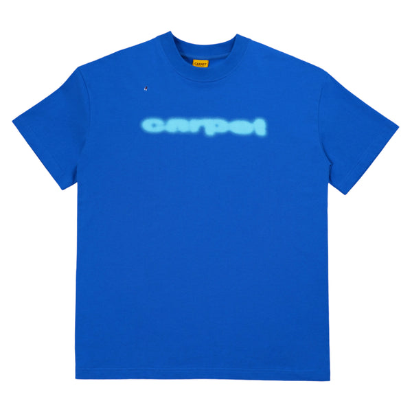 A blue T-shirt with "CARPET" printed in a blurry white font across the chest and a small logo near the collar. Known as the Carpet Co. Carpet Fly Tee Blue, it's perfect for casual outings with a touch of quirky charm.